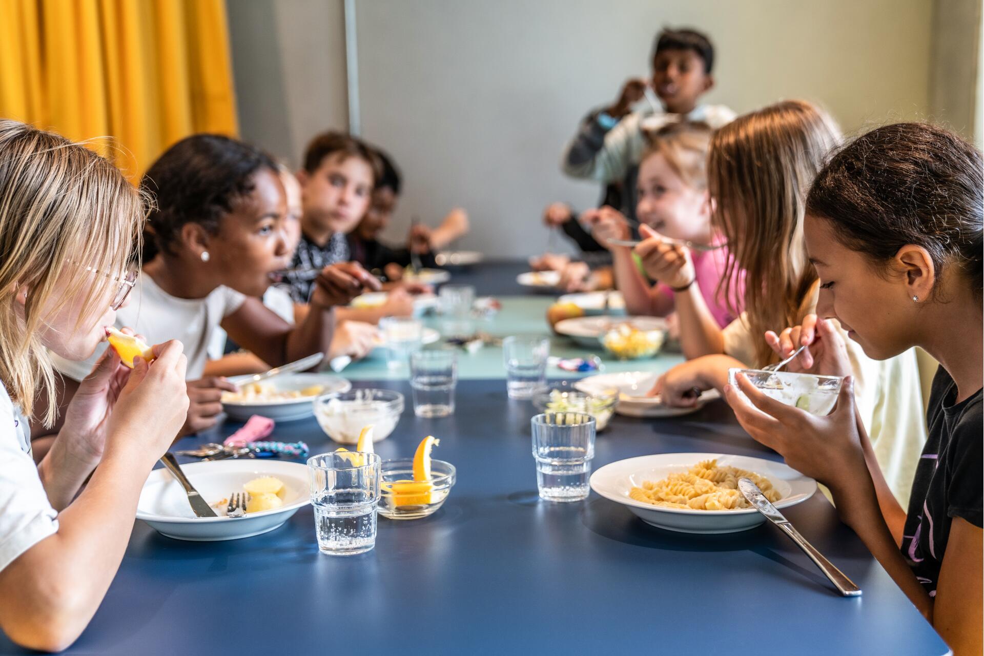 Kinder essen zusammen an einem Tisch, lachen und genießen ihr Essen