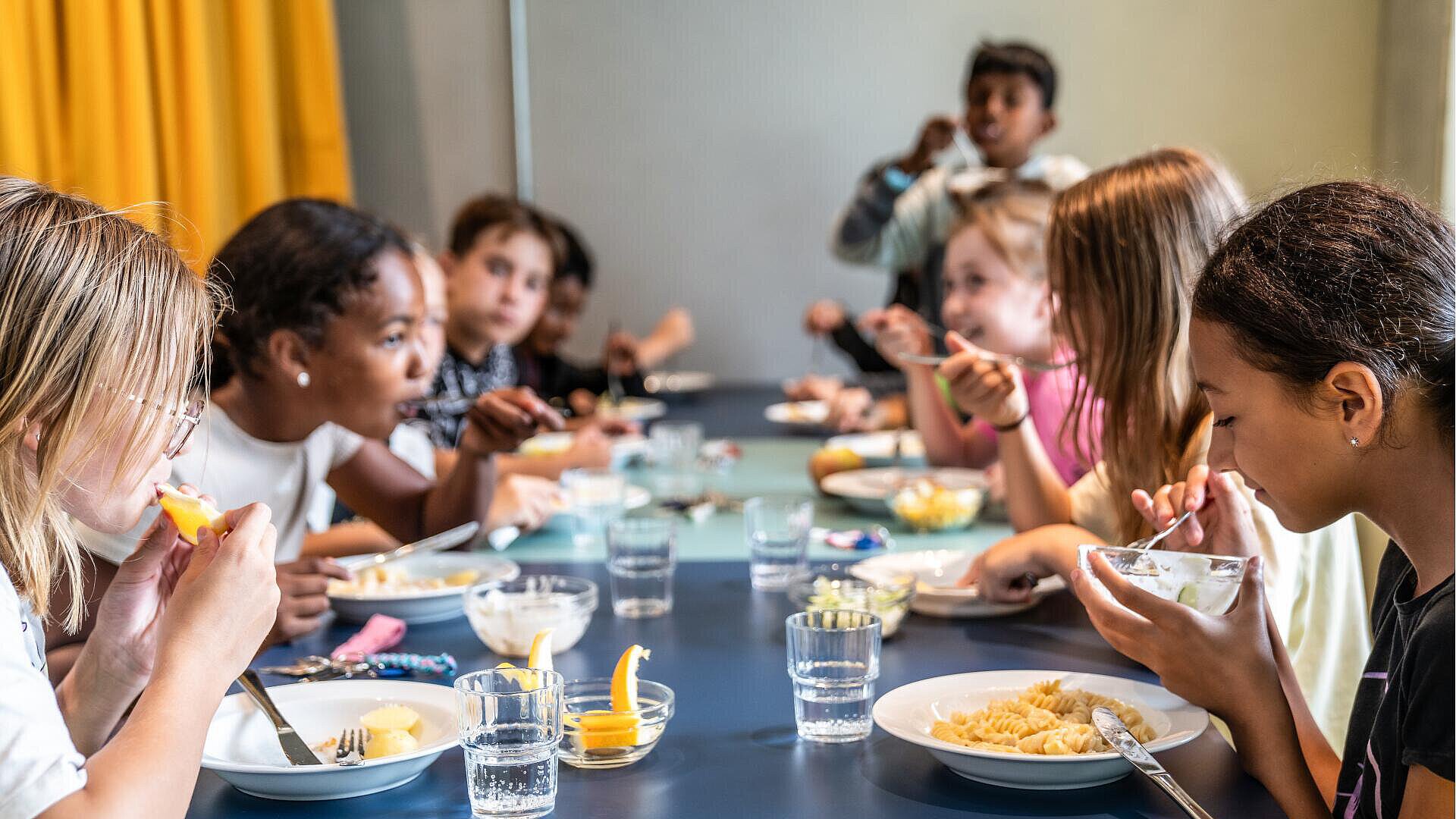 Kinder essen zusammen an einem Tisch, lachen und genießen ihr Essen
